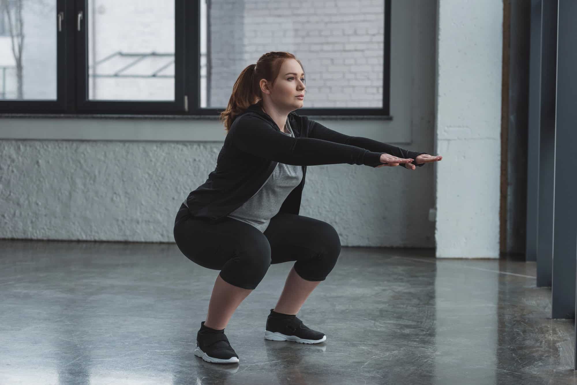 Woman doing bodyweight squats with proper form in a female beginner workout plan