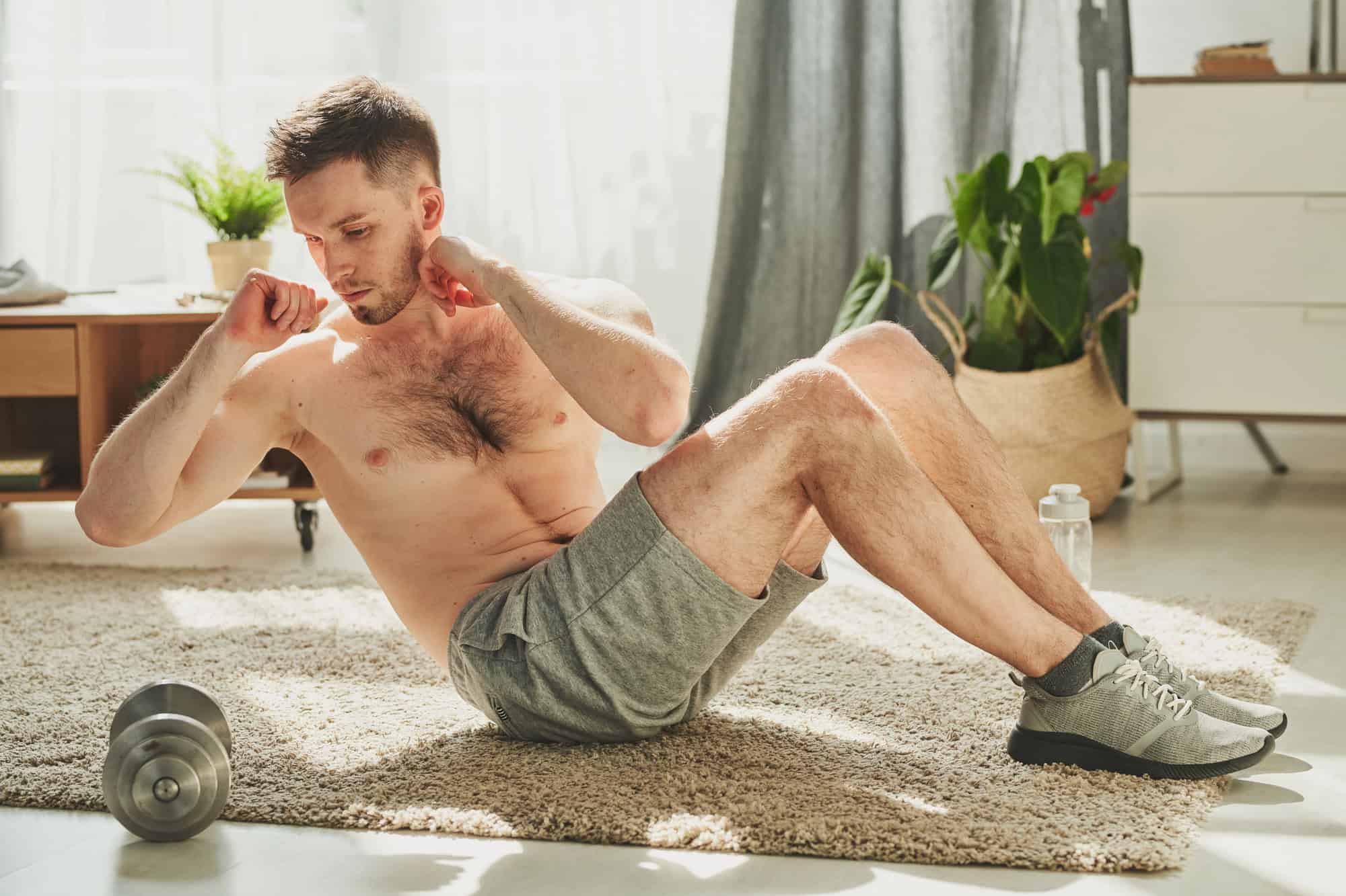 Man demonstrating proper sit-up form on a carpeted floor as part of a beginner calisthenics workout plan