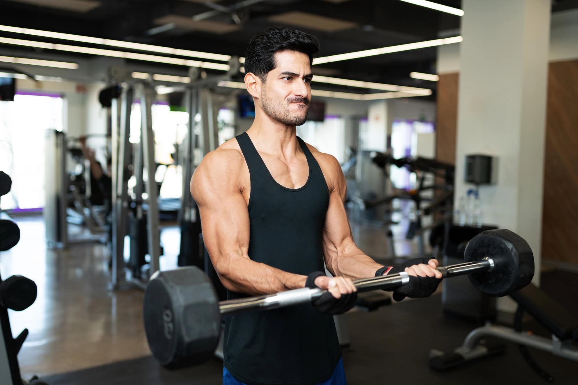 Man performing standing barbell curls during a gym arm workout for muscle growth