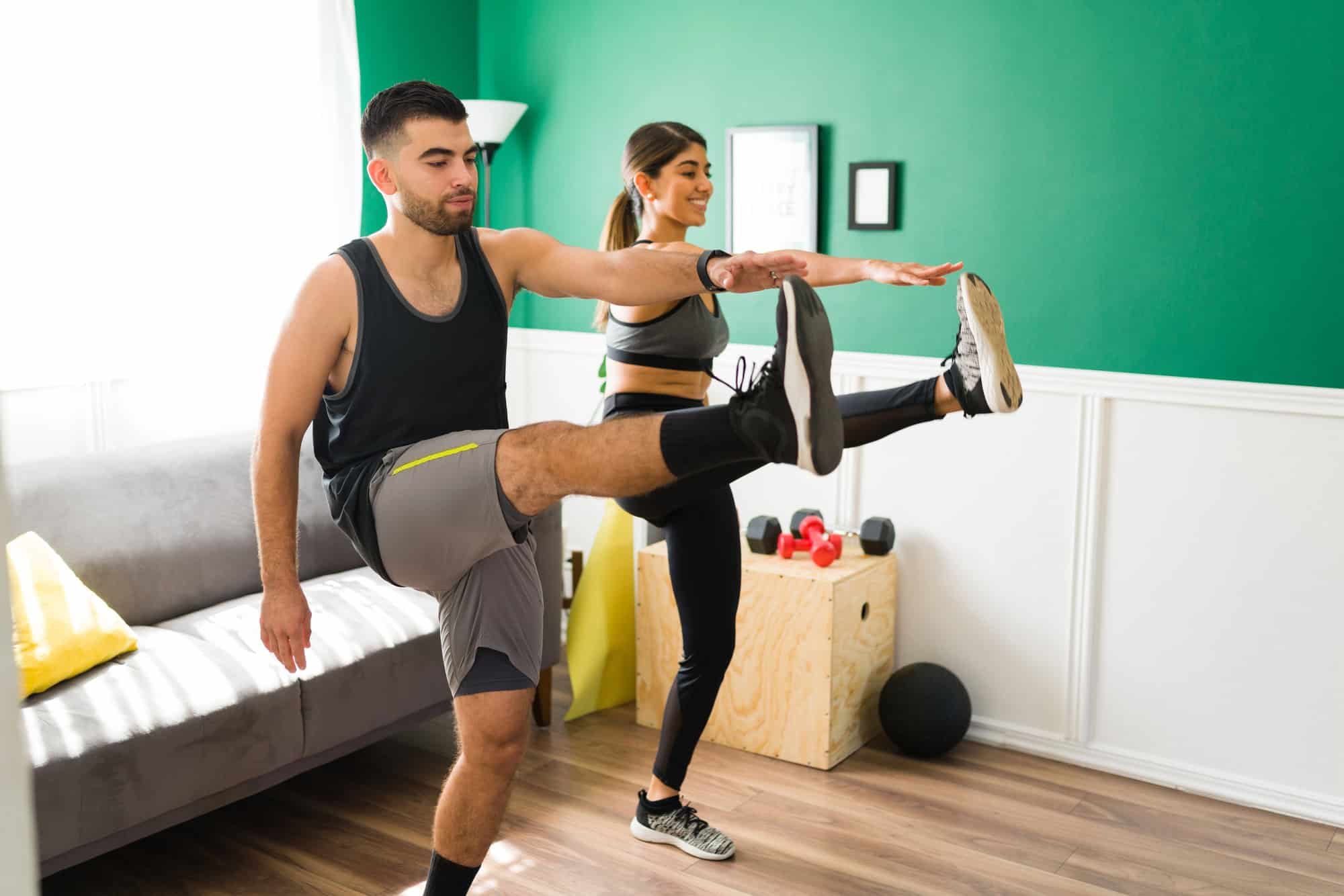 Man and woman doing high kicks at home as part of a bodyweight HIIT workout without equipment