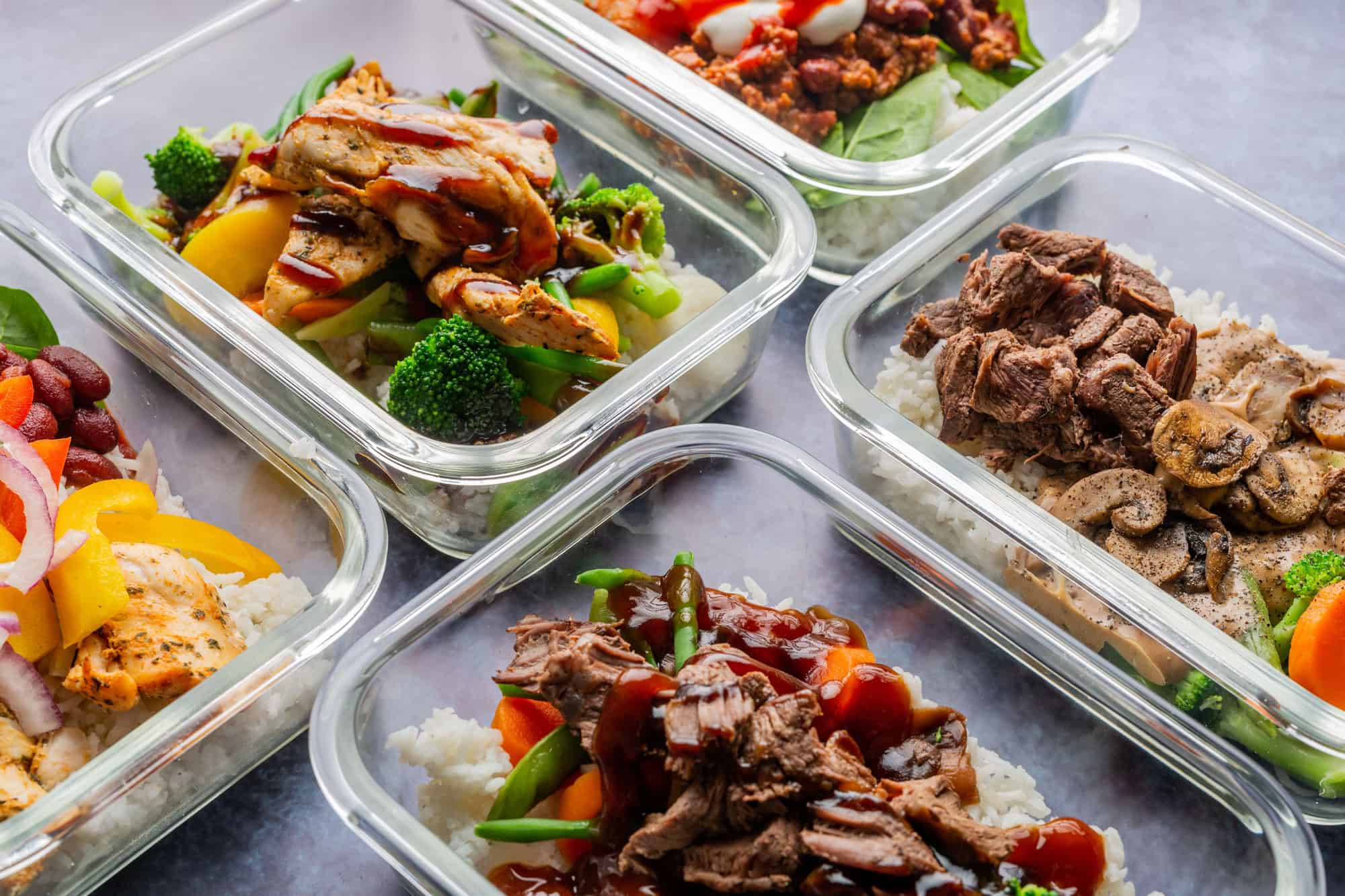 Glass meal prep containers filled with rice, veggies, and meat options for easy and cheap high protein meals