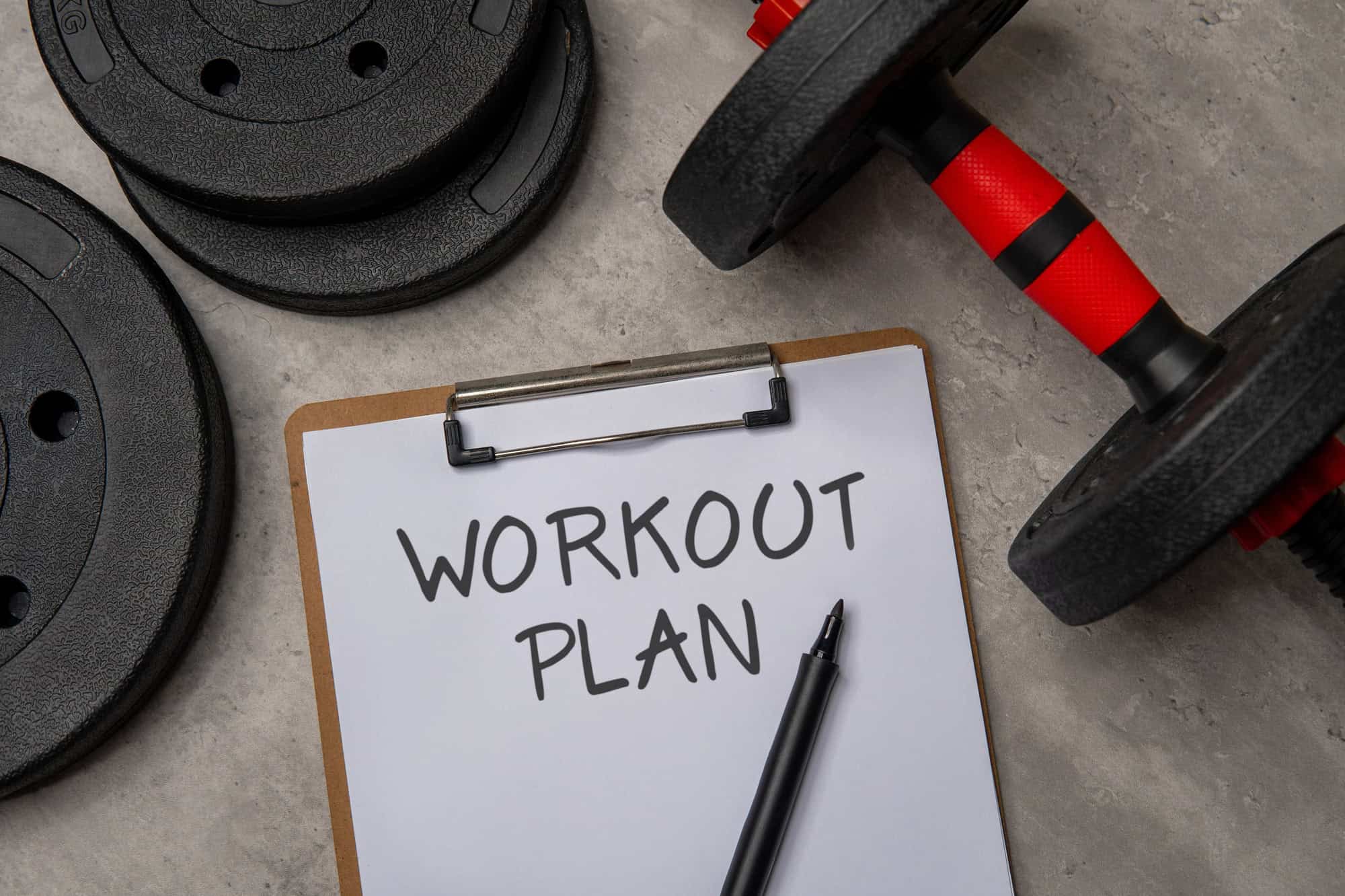 Workout plan written on paper with dumbbells and weight plates nearby, representing a 6 day gym workout schedule