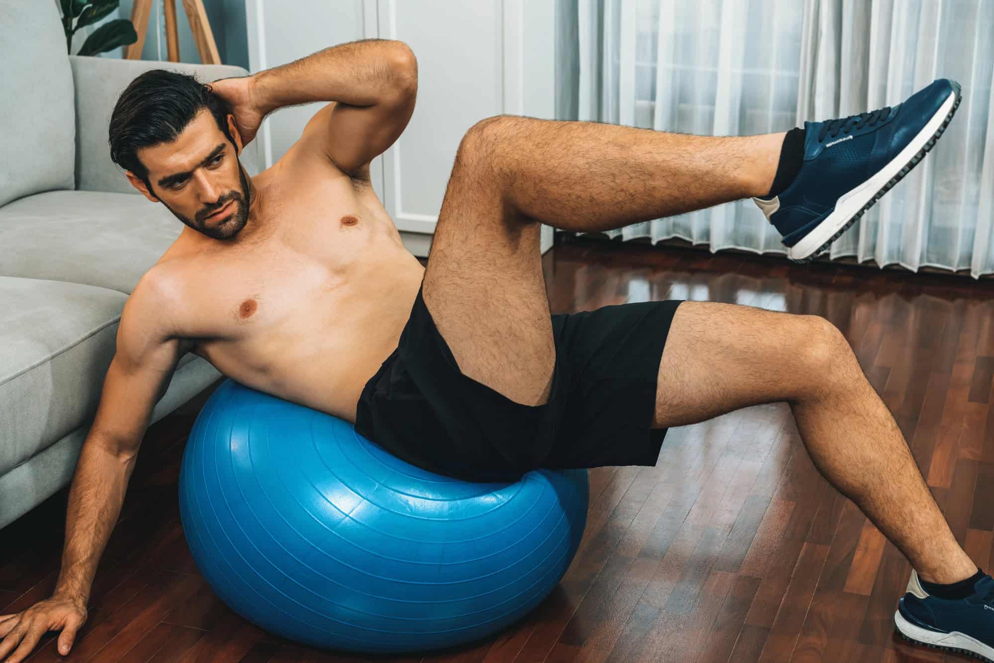 Full Body Exercises – Core and Balance Training on Stability Ball Man performing a full body exercise on a stability ball as part of a 6 day gym workout schedule to engage core, legs, and upper body