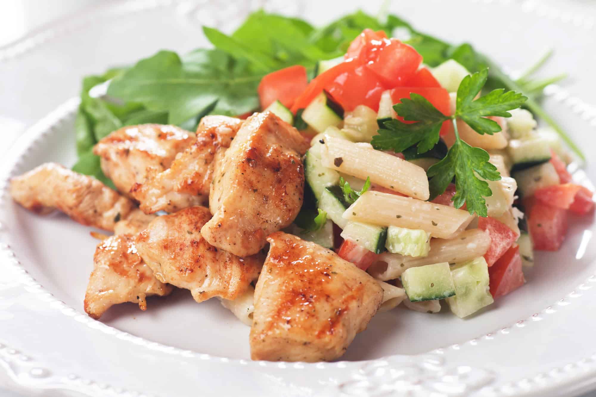 Plate of grilled chicken, pasta salad, and greens served as an easy high protein lunch option
